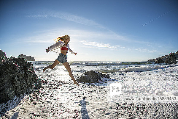 Teenager-Mädchen springt am Strand vom Felsen in die Brandung