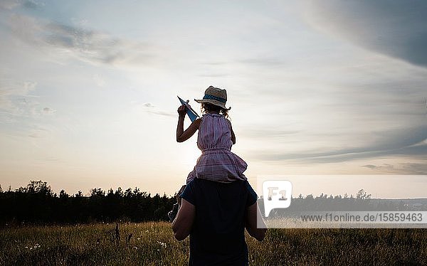 father carrying his daughter on his shoulders walking at sunset