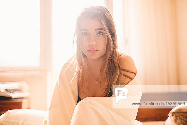 Portrait of young woman sitting in bed at home