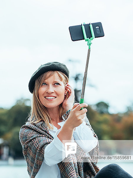 Kaukasisches Mädchen mit französischem Hut fotografiert sich selbst mit einem Selfie-Stock