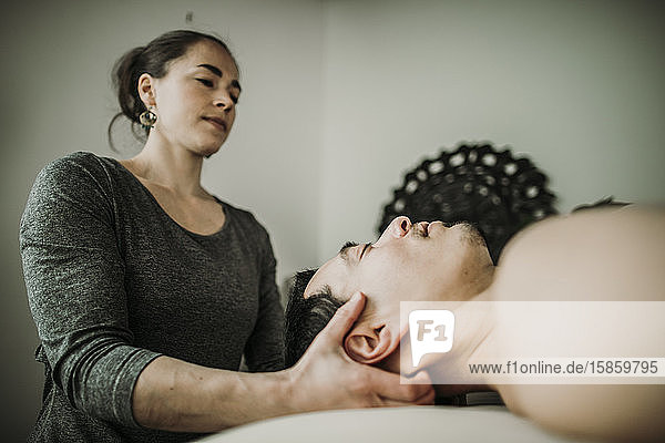 männlicher Massagepatient lässt Nacken von weiblicher Masseurin bearbeiten
