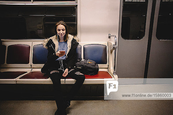 Young happy woman using smart phone while traveling in subway train