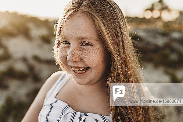 Portrait of young smiling redhead girl with freckles at beach sunset