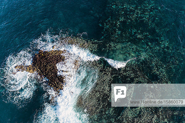 Luftaufnahme einer Welle  die sich über einem scharfen Lavariff auf Teneriffa bricht.