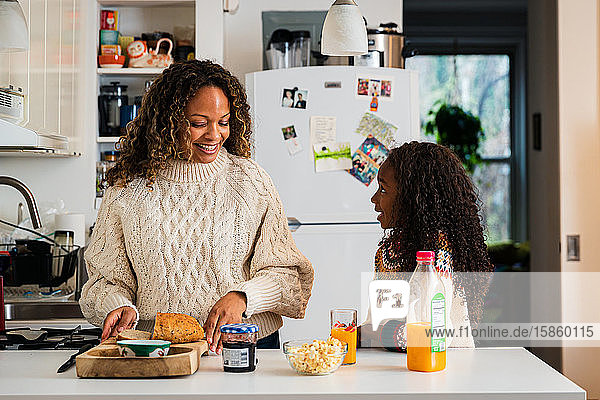 Mädchen im Gespräch mit lächelnder Mutter  die zu Hause in der Küche das Frühstück vorbereitet