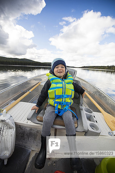Young boy sitting in aluminum boat during fishing trip.