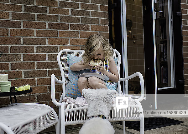 Mädchen isst draußen  während ihr Hund sehnsüchtig nach Futter sucht