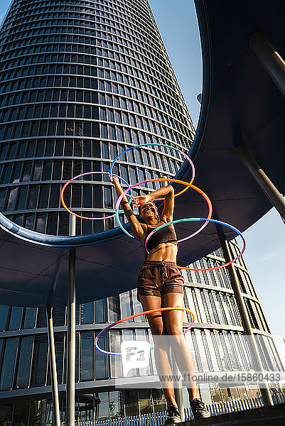 Glückliche Frau führt Hula-Hoop-Tanz mit fünf Ringen im Stadtgebiet auf