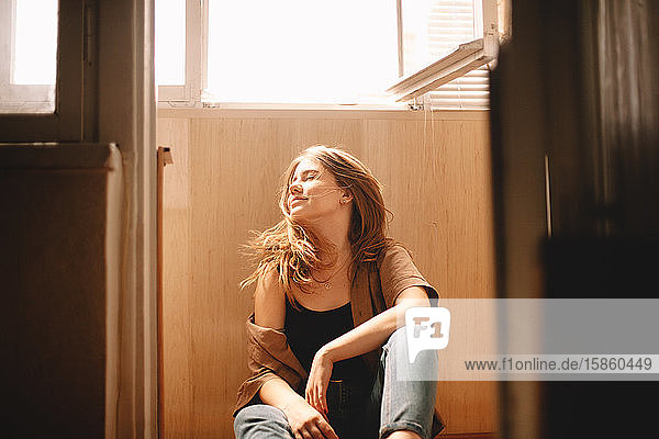 Junge Frau  die im Sommer auf dem Boden sitzend auf dem Balkon Haare wirft
