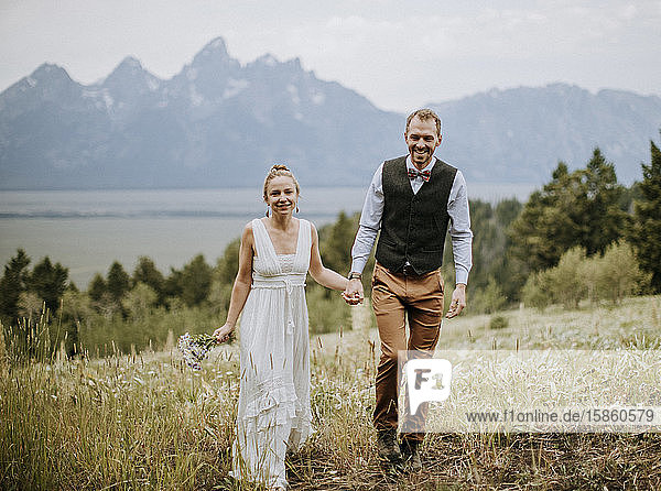 Braut und Bräutigam gehen durch ein Wildblumenfeld vor den Bergen