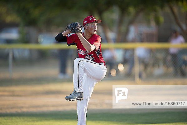 jugendlicher Baseball-Pitcher in roter Uniform in vollem Wind auf dem Hügel