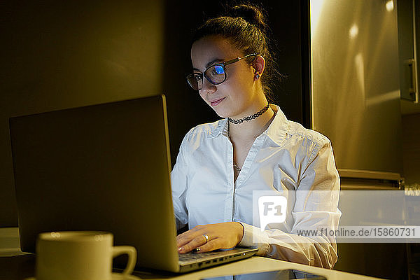 Junge Frau  die abends mit dem Laptop arbeitet