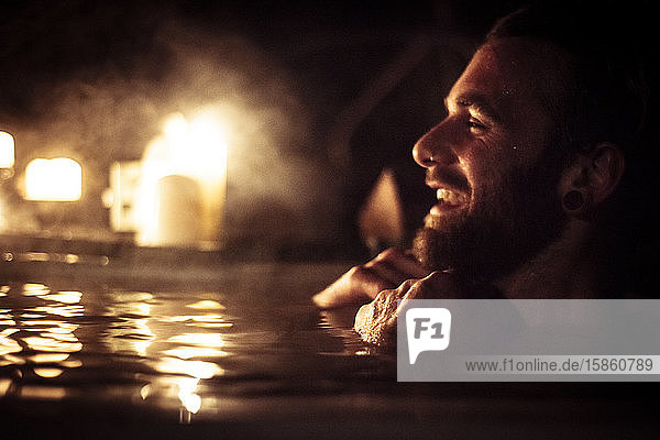 Mann im Whirlpool lächelt bei Kerzenlicht und Dampf