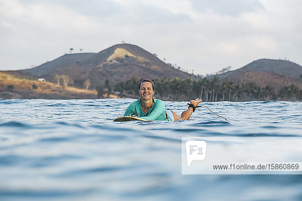 Lächelnde junge Frau auf dem Surfbrett liegend