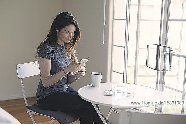 Textnachrichten von Frauen auf Smartphones  während sie im Wohnzimmer Kaffee am Tisch am Fenster trinken