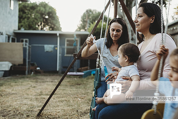 Two moms with baby and 5 yr old on swingset playing with bubbles