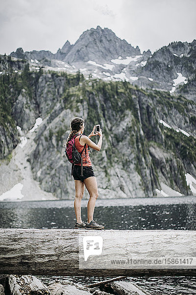 Eine Wanderin macht beim Wandern entlang eines Sees ein Zellenfoto
