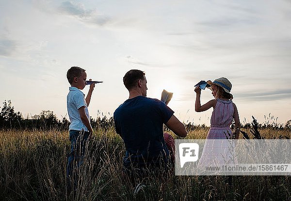 Vater spielt mit seinem Sohn & seiner Tochter bei Sonnenuntergang Papierflieger