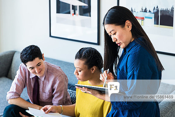 Businesswoman using graphics tablet while coworkers discussing over documents in office