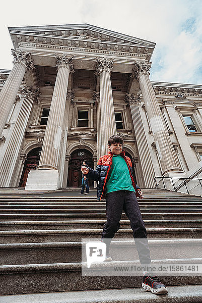 Young boy running down steps of a big stone building in New York City.