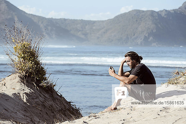 Mann benutzt Smartphone am Strand
