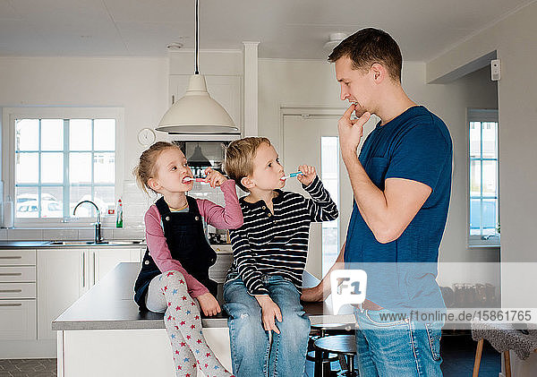 father teaching his kids how to brush his teeth before school
