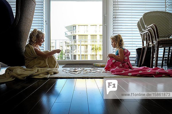 kleine Mädchen  die in Decken auf dem Boden sitzen und im Gegenlicht Karten spielen