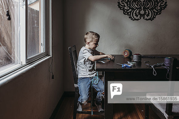 Junge Junge strickt zu Hause während der Isolation mit den Fingern
