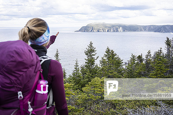 Female Backpacker Points At Cove On East Coast Trail In Newfoundland