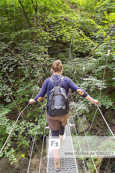 Hiker crossing metal suspension bridge on hiking trail.