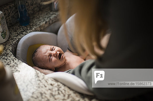 Weinende Neugeborene  die zum ersten Mal zu Hause ein Bad im Waschbecken nehmen