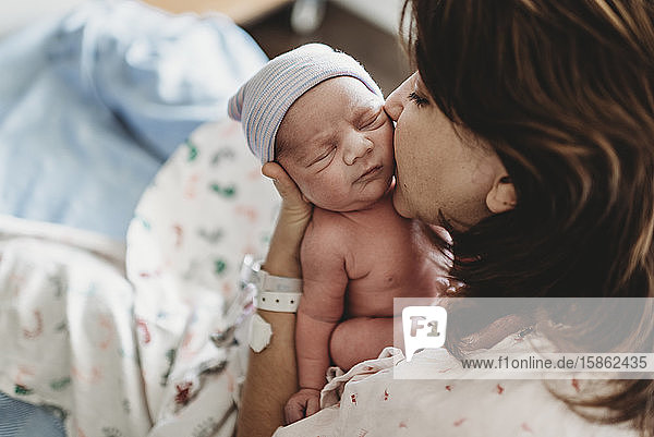 Close up detail of mother kissing newborn son's cheek in hospital