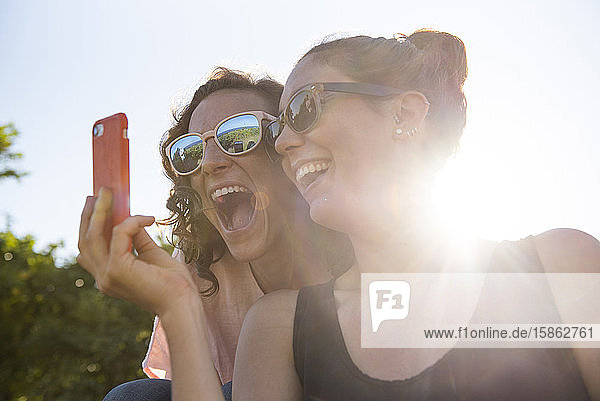 Zwei Freundinnen lächeln für ein Selfie im Sonnenschein.