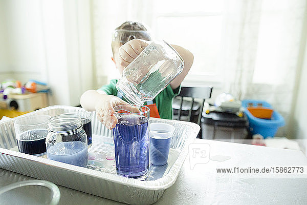Anonymes Kind gießt während eines wissenschaftlichen Experiments blaue Flüssigkeit in Glas