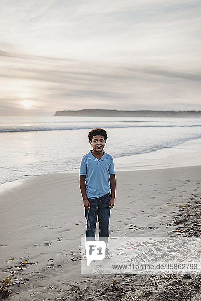 Porträt eines jungen Jungen im Schulalter  der bei Sonnenuntergang am Strand lächelt