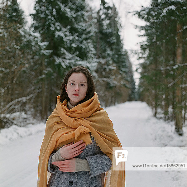 Woman stands in a winter forest with a yellow scarf