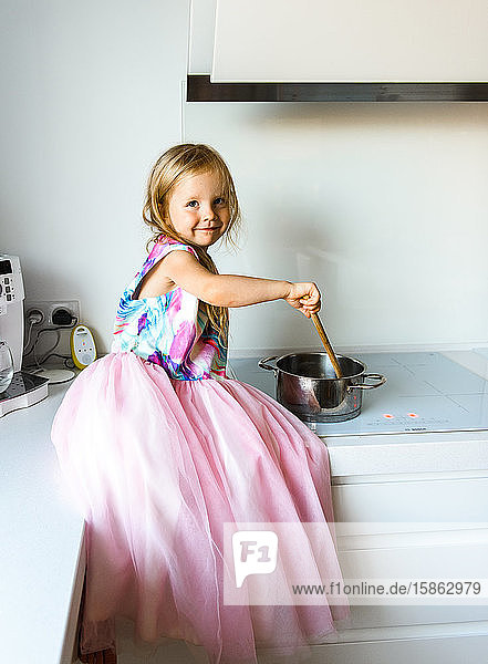 Little girl in elegant dress sitting on a table in the kitchen