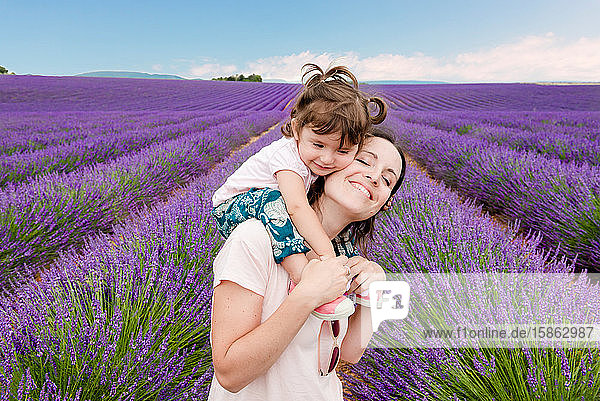 Glückliche Frau und kleines Mädchen spazieren im Sommer zwischen Lavendelfeldern