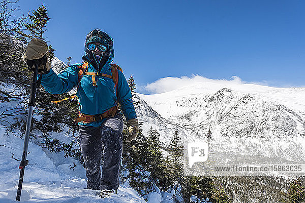 A woman hiking alone down a snowy slope with Tuckerman Ravine and the summit of Mount Washington in the background.
