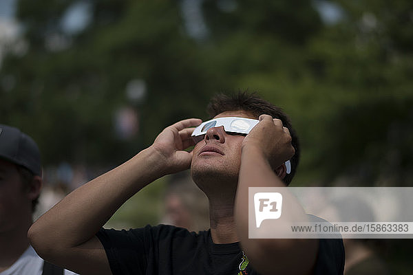 Junger Mann schaut zur Sonnenfinsternis auf und trägt eine Papierschutzbrille