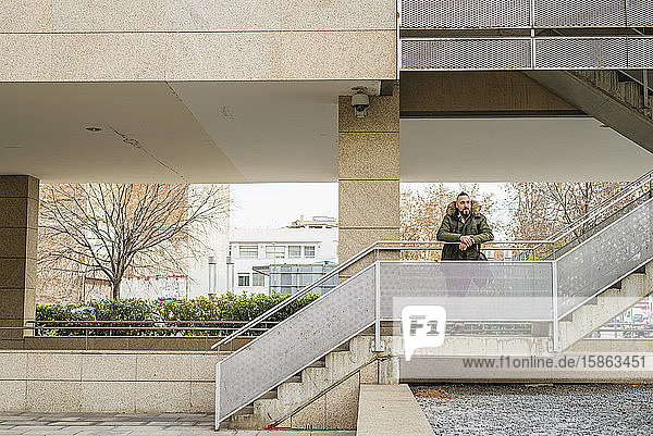 Bärtiger Hipster-Mann entspannt sich auf einer Treppe in einem Gebäudekomplex