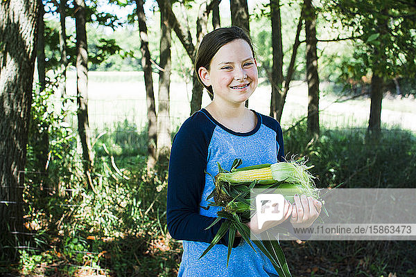 Mädchen lächelt  während sie einen Arm voll Zuckermais hält