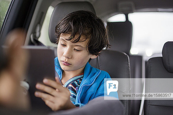 A boy sits in a carseat on a car trip watching a tablet