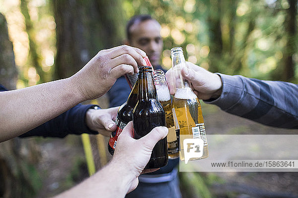 Männer jubeln im Wald ihren Bierflaschen zu.