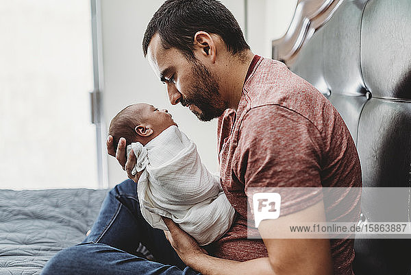 Mid-30â€™s dad with beard admiring newborn wrapped in white blanket