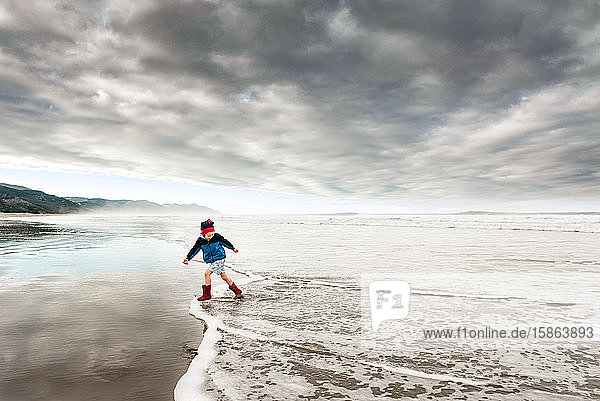 Child running in water at New Zealand beach on cloudy afternoon
