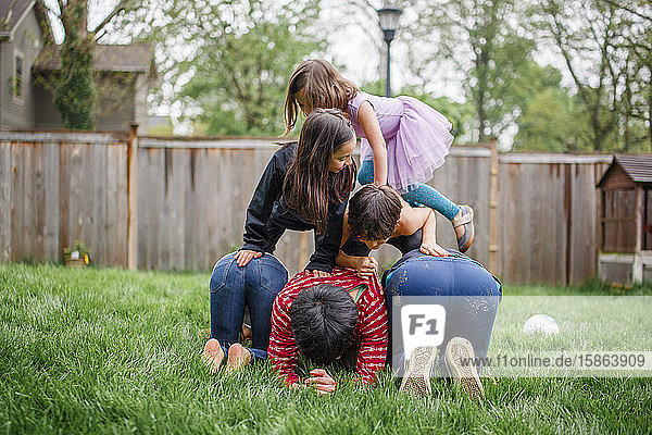 Two adult brothers build a human pyramid with their children outside