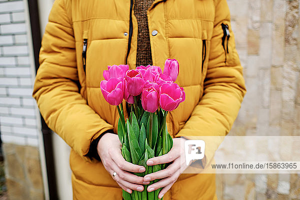 blonder Mann in einer gelben Winterjacke mit einem Tulpenstrauss in den Händen