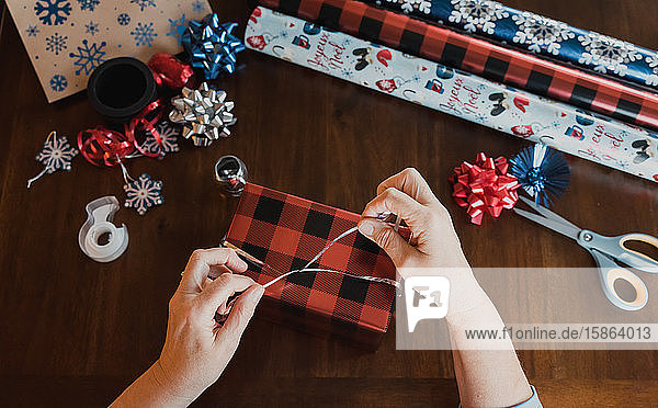 Hands wrapping present at wooden table with gift wrapping supplies.
