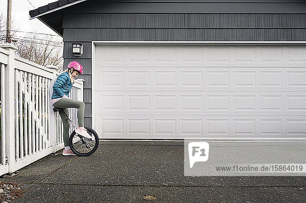 Mädchen mit rosa Helm schaut auf das Einrad vor dem Garagentor